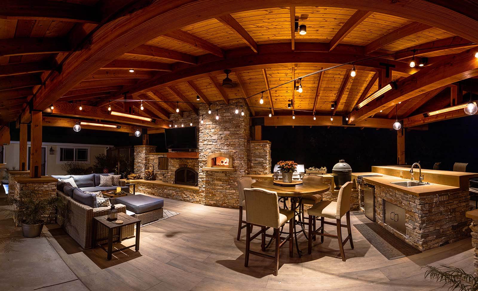 Residential outdoor kitchen featuring dining area, stone countertops, and covered gathering space by K&D Landscaping