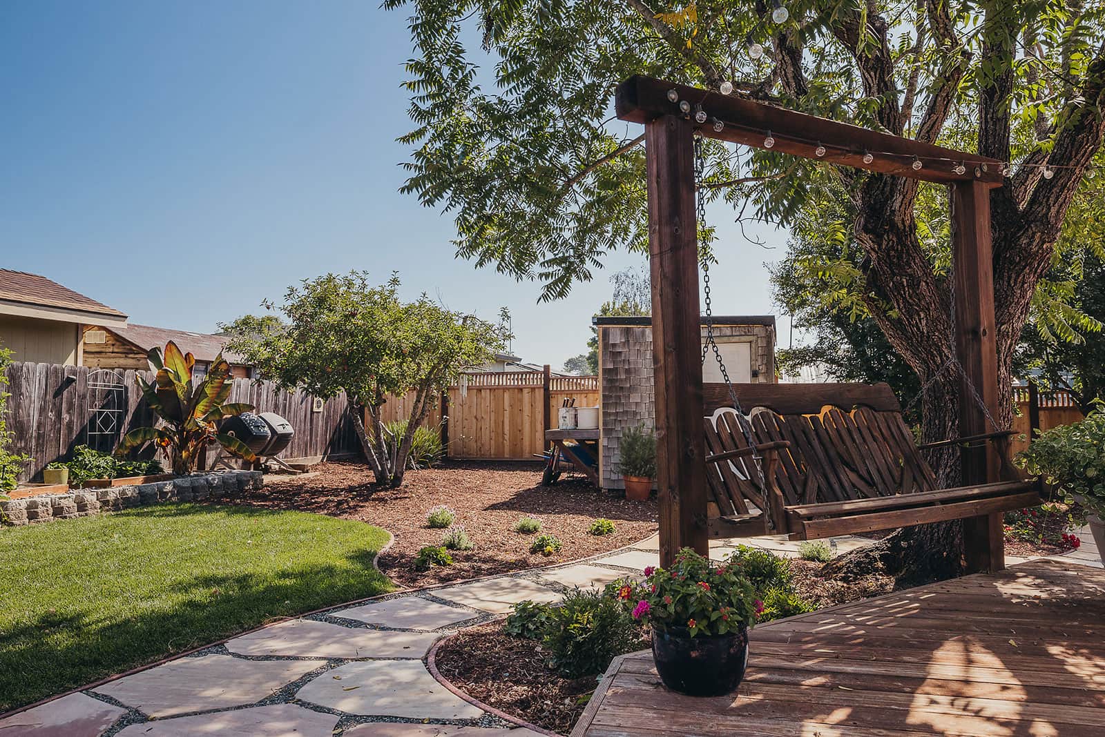 Residential yard with modern pergola structure, stepping stone pathway, mature tree canopy, and lawn entertaining space by K&D Landscaping