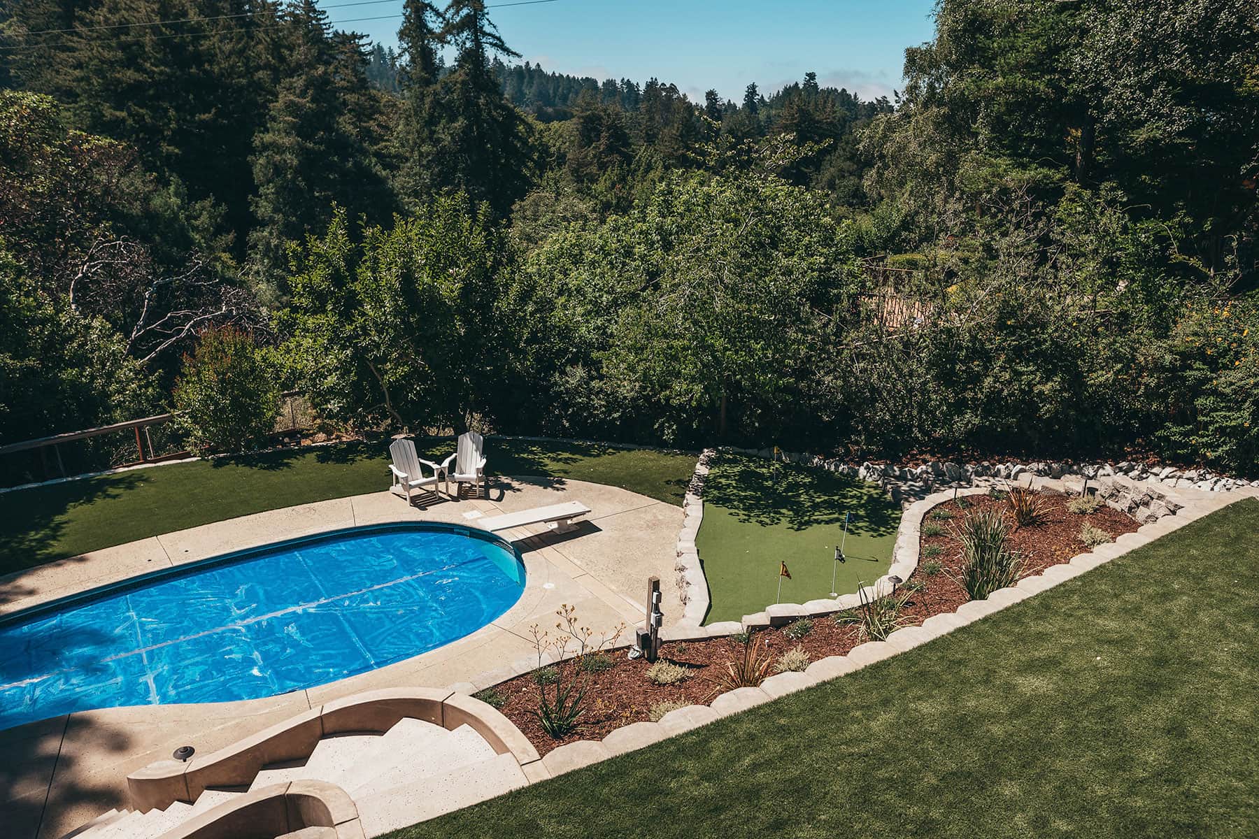 Resort-style backyard oasis with swimming pool, putting green, spacious lawn, and forest setting created by K&D Landscaping in Scotts Valley