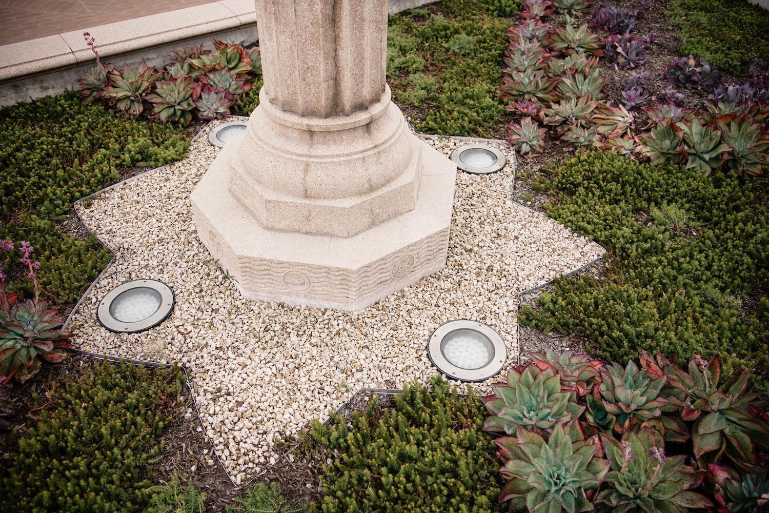 Stone column base detail with surrounding gravel, landscape lighting, succulents, and low plantings installed by K&D Landscaping