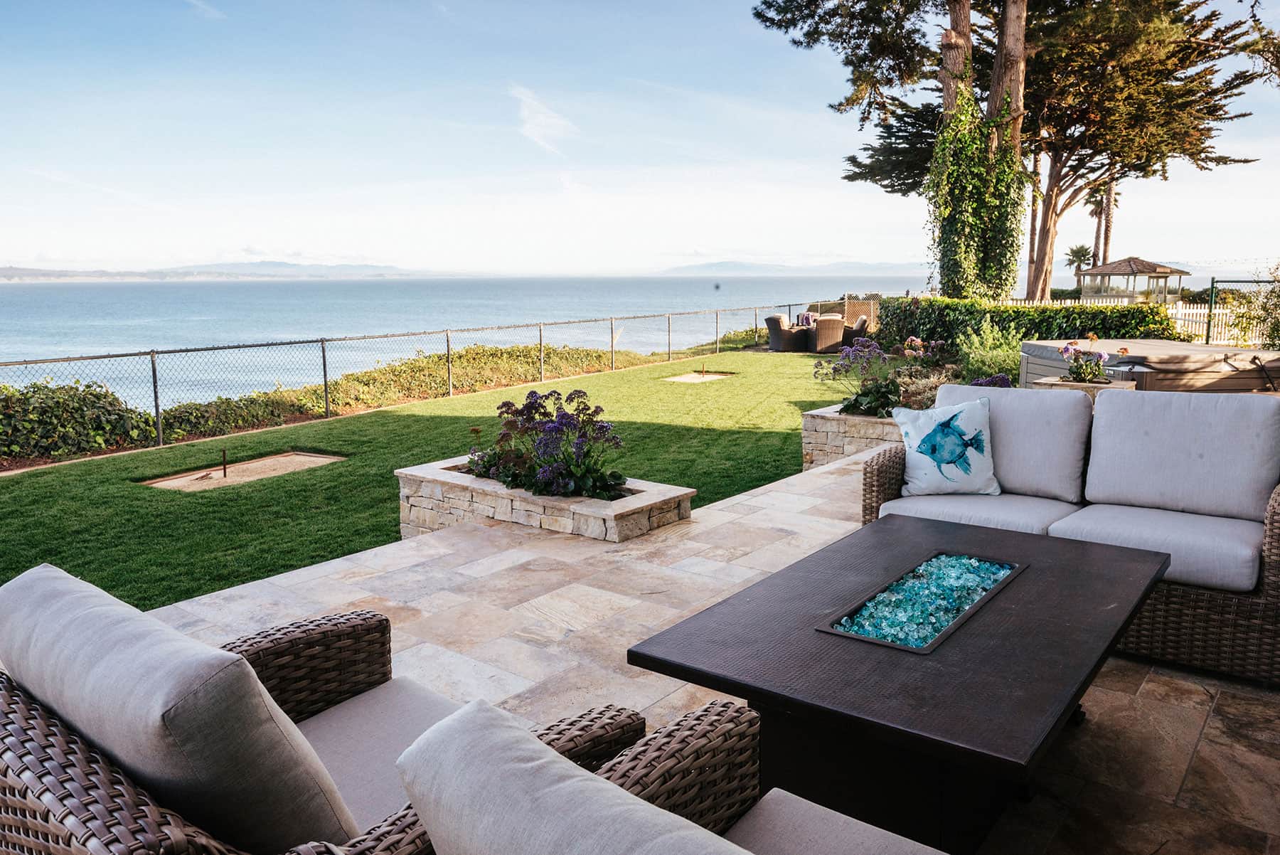 Wicker patio seating with fire table & coastal views by K&D Landscaping